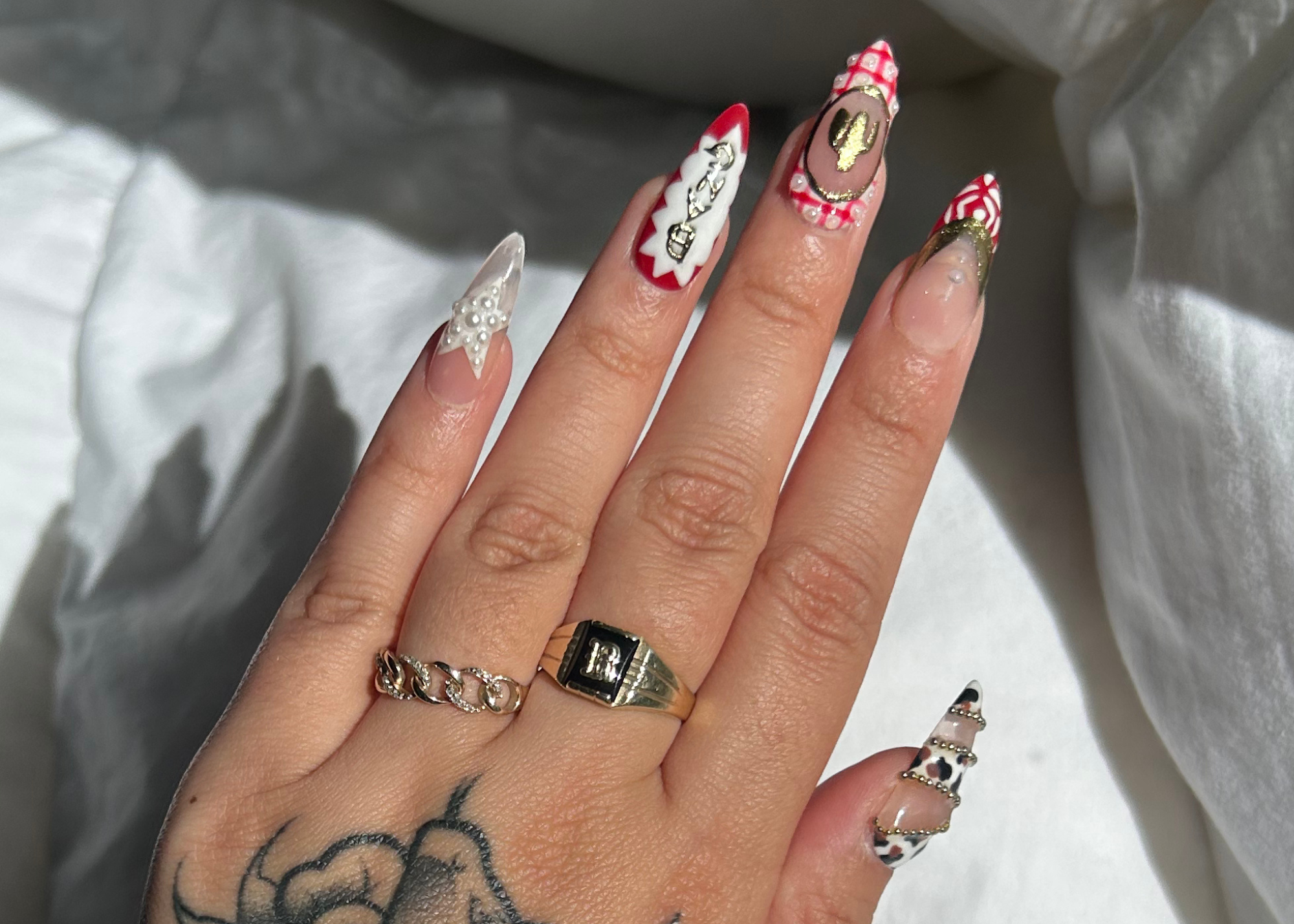 Hand with intricately designed nails and tattoos on a white fabric background